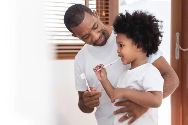 快乐的非裔美国家庭 爸爸教他的儿子穿白衬衫一起在浴室刷牙 父亲和小孩 卷曲的头发 享受着家中的牙齿卫生 — 图库照片