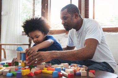 Afrikalı bir aile baba ve oğlu evde oturmuş oyun oynuyorlar. Mutlu Kara Baba ve çocuk renkli tahta bloklardan kule yapıyorlar. Geliştirme, Öğrenme ve Eğitim kavramı.