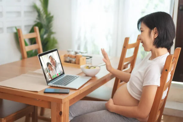 自宅のノートパソコンでビデオ通話をするアジアの妊婦 懐妊中のお母さんは笑顔でノートにシニア男女に手を振って話していました インターネットワイヤレスで幸せな家族 — ストック写真