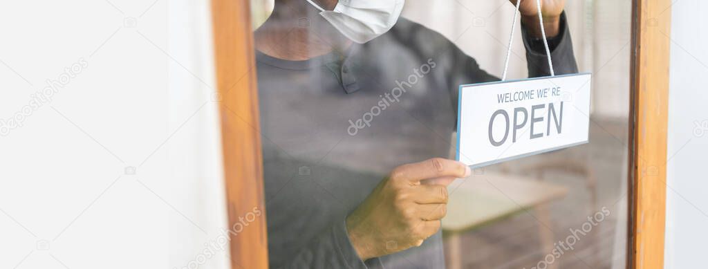 Black male holding open sign at the door. African American cafe man owner with face mask reopening after coronavirus epidemic quarantine. Startup small business after Covid-19, Banner