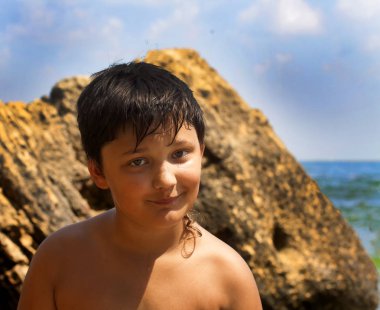 Deniz ve taşların arka planda gülümseyen çocuk.
