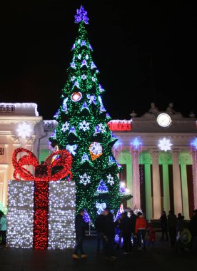 Noel ağacı ve kırmızı fiyonklu büyük bir hediye kutusu. Yeni Yıl Noel'i. Kar taneleri, süslemeler.