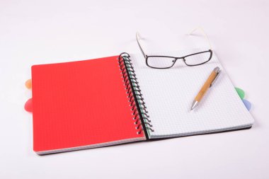 Hafif arka planda kalem ve gözlüklü bir defter aç. Kırmızı kartı olan bir defter..