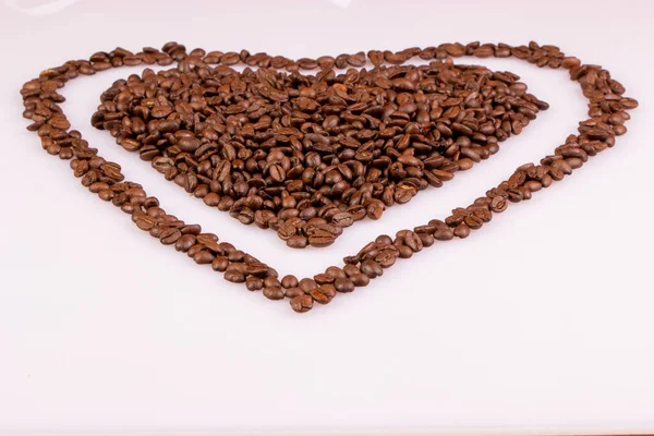 Roasted coffee beans arranged in a heart shape over light background. Heart with a border.