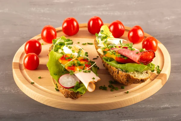 Sandwiches with vegetables, ham, tomatoes, egg on a wooden table and a gray background. Tomatoes in the background.