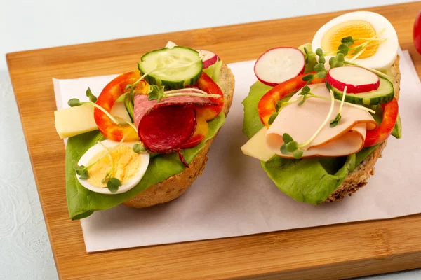 Sandwiches with vegetables, ham, tomatoes, egg on a wooden table and a light background. Tomatoes in the background.