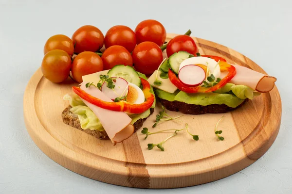 Sandwiches with vegetables, ham, tomatoes, egg on a wooden table and a light background. Tomatoes in the background.