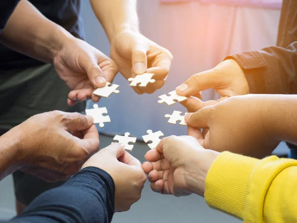 Close-up of many young people hands holding jigsaw puzzle pieces in circle together with sunlight effect.