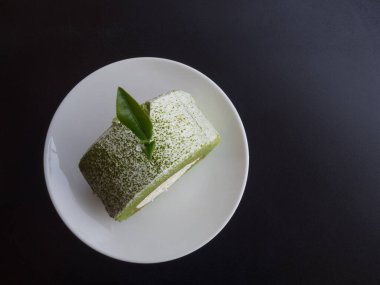 Beyaz tabak ve siyah arkaplanda yeşil çay kekinin üst görüntüsü. Metin için boşluk.