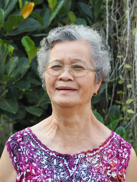 Portrait of an elderly woman wearing eyeglasses, smiling and looking at camera while standing in a garden. Space for text. Concept of old people and healthcare