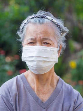 Bahçede dururken maske takan yaşlı bir kadının portresi. Virüsü, bakteriyi, polen tanelerini korumak için maske. Yaşlılar ve sağlık hizmetleri kavramı