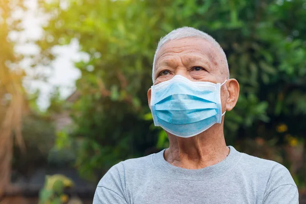 Bahçede dururken maske takan yaşlı bir adamın portresi. Virüsü, bakteriyi, polen tanelerini korumak için maske. Yaşlılar ve sağlık hizmetleri kavramı