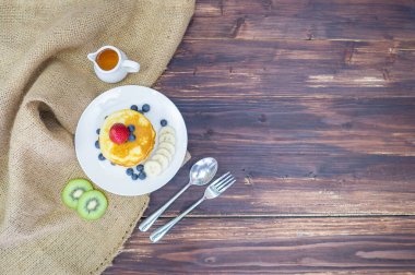 Taze yaban mersinli krep, muz dilimi, çilek ve ahşap masada karamel şurubu.