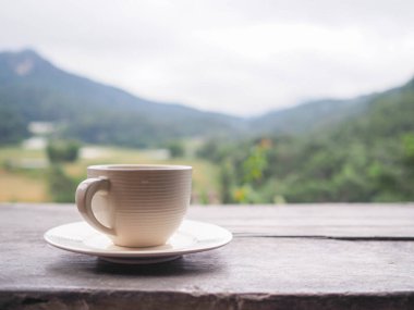Bir fincan kahve ahşap masada dinleniyor. Arka planda güzel bir dağ manzarası ve metin için yeri var.