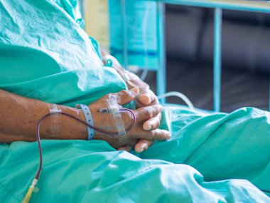 Üst düzey bir hastanın eli hastada anemi tedavisi sırasında kan veriyor. Hastanede yatağında oturan Asyalı yaşlı bir hasta. Sağlık hizmetleri danışmanı