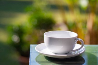 Bahçede doğa arka planı olan tahta masanın üzerinde beyaz bir fincan kahve. Metin için boşluk