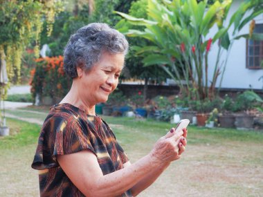 Elinde akıllı bir telefonla bahçesinde gülümseyen son sınıf öğrencisinin portresi. Rahatlamak için çok güzel bir doğa. Sağlıklı konsept