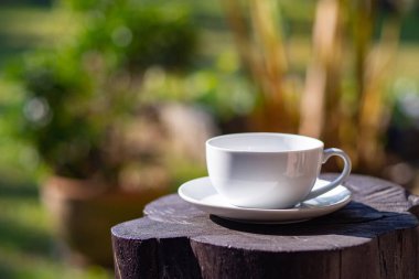 Bahçede doğa arka planı olan tahta masanın üzerinde beyaz bir fincan kahve. Metin için boşluk