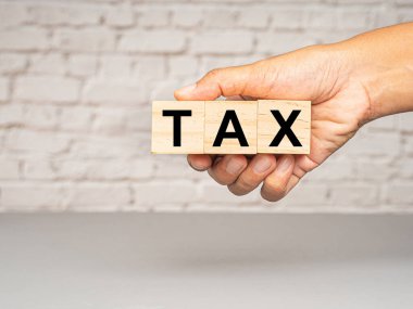 Vergi günü konsepti. Tahta bir küpün el ele tutuşması. Beyaz tuğlalı arka planda TAX harfleri var.