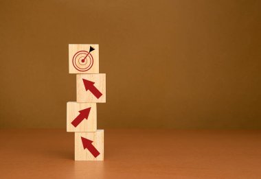 İş büyümesi konsepti. Kırmızı okları olan tahta küpler, mermer zemin üzerinde mavi arkaplan olan bir dart simgesini işaret ediyor. Bir hedefe odaklan ve başarılı bir işe ulaş.