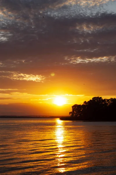 Horizontal landscape photography of an adorable warm orange summer sunset above the sea with dark silhouette of unknown island, calm water and dark clouds in the sky on the background