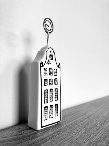 Monochrome photography of an isolated ceramic photo holder made like apartment building standing on the wooden surface with white wall on the background