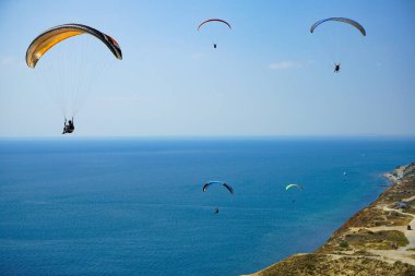 Paragliderler güzel yamaç paraşütleri üzerinde süzülür mavi gökyüzü ve mavi denizin arka planına karşı, dağların tepesinden çekilen