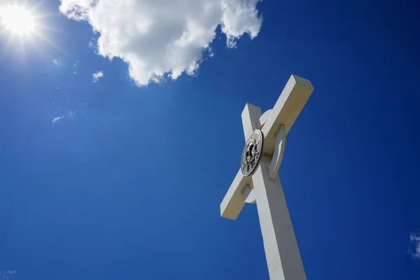 white chrestian cross on a background of blue sky, white clouds and sunbeams