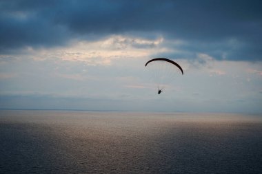 Gün batımında denizin üzerinde bir paraglider uçar. Karanlık deniz ve kara bulutlar arasında, gökyüzünün aydınlık kısmına karşı.