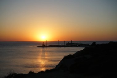 Gün batımında adada deniz feneri ve batan güneşin ışığında denizde güzel bir gölge.
