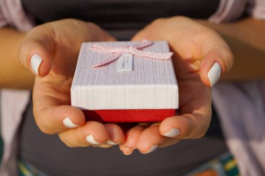 Bir kadın, bakımlı manikürlü güzel ellerde küçük bir hediye kutusu tutar. Kız dışarıda, siyah bir tişörtün üzerine açık renk bir gömlek giyiyor.