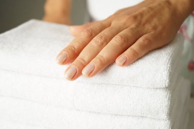 Güzel elleri ve güzel manikürlü bir kadın temiz katlanmış beyaz havlu yığınını içeride tutuyor.