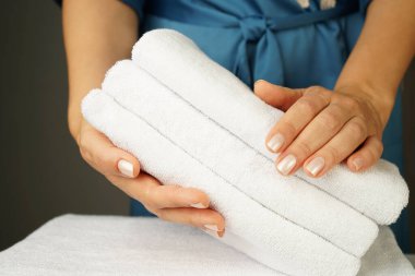 Turkuaz ipek bornozlu, güzel elleri ve güzel manikürlü bir kadın, güzelce katlanmış beyaz havlu yığınını içeride tutuyor.