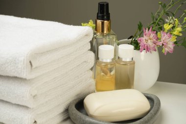Komodinin üzerinde bir duş seti, temiz beyaz terry havlular, birkaç şişe duş jeli ve şampuan, taş sabun kabında sabun ve güzel bir demet çiçek.