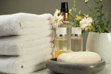 Komodinin üzerinde bir duş seti, temiz beyaz terry havlular, birkaç şişe duş jeli ve şampuan, taş sabun kabında sabun ve güzel bir demet çiçek.