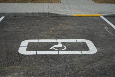 Asfalttaki engelli işareti için park alanı beyaza boyanmış ve kaldırımın çıkış noktası sarıya boyanmış.