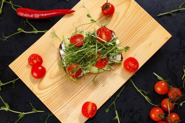 Domateslerle çevrili ahşap bir tahtanın üzerinde mikro yeşillikli bir sandviç.