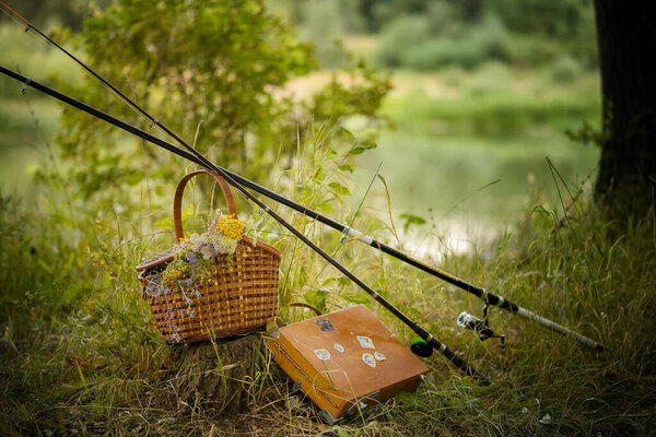 set for picnic and fishing, romantic evening two fishing rods, a basket of flowers on the background of the river 