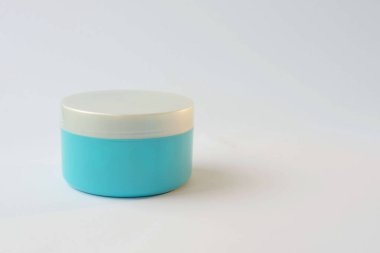 Beyaz arka planı gri kapaklı bir mavi krema kavanozu.