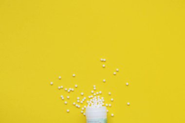 Homeopatik küreseller ve sarı arka planda plastik bir kavanozla. Alternatif Homeopati ilaç şifalı bitkiler, sağlık sigortası ve hap konsepti. Flatlay. Üst Manzara. metin için metin boşluğu. Çocuklar için Homeopati