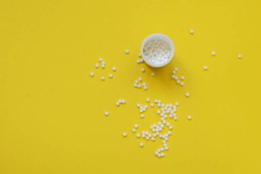 Homeopatik küreseller ve sarı arka planda plastik bir kavanozla. Alternatif Homeopati ilaç şifalı bitkiler, sağlık sigortası ve hap konsepti. Flatlay. Üst Manzara. metin için metin boşluğu. Çocuklar için Homeopati