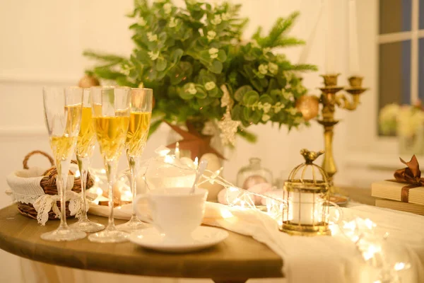 Yumuşak odaklı yeni yıl atmosferi. Yılbaşı gecesi. Beyaz bir masanın üzerinde 4 bardak şampanya ve bir de çelenk. Noel masası. Noel gecesi evde