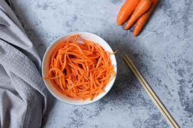 Taze ve sağlıklı sebzeler Kore salatası beyaz tabakta rendelenmiş havuç. Sağlıklı beslenme ve vejetaryen gıda konsepti. Sebzeler ve aşçılık geçmişi. Üst Manzara. Organik baharatlı havuç salatası..