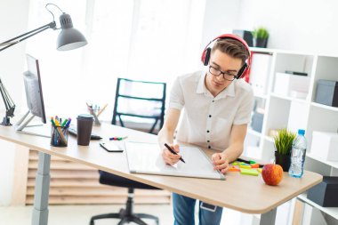 Gözlüklü ve kulaklıklı genç bir adam manyetik tahtaya bir işaret çizer..