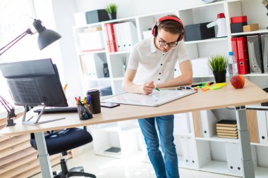 Gözlüklü ve kulaklıklı genç bir adam manyetik tahtaya bir işaret çizer..