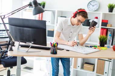 Gözlük ve kulaklık genç bir adamla bir bardak kahve elinde tutuyor ve bir işaretleyici tahtaya çizer.