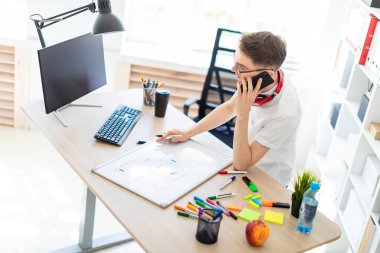 Gözlüklü genç bir adam bir bilgisayar masası duruyor ve telefonda konuşuyor. Önce onu bir manyetik kurulu ve işaretleri yatıyor. Çocuklar kulaklık boynuna asmak.