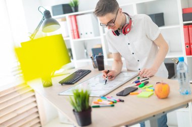 Gözlüklü genç bir adam bir bilgisayar masası duruyor. Genç bir adam bir işaretleyici manyetik bir tahtaya çizer. Çocuklar kulaklık boynuna asmak.