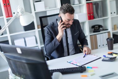 Bir adam masada, ofisinde oturuyor telefonda konuşurken ve belgeleriyle çalışma.