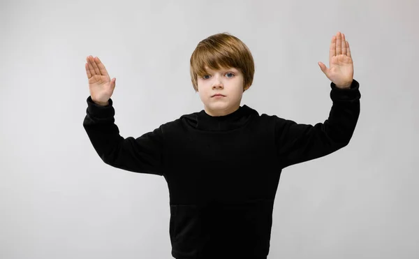 Retrato de adorable niño serio de pie en el estudio con las manos en alto sobre fondo gris — Foto de Stock